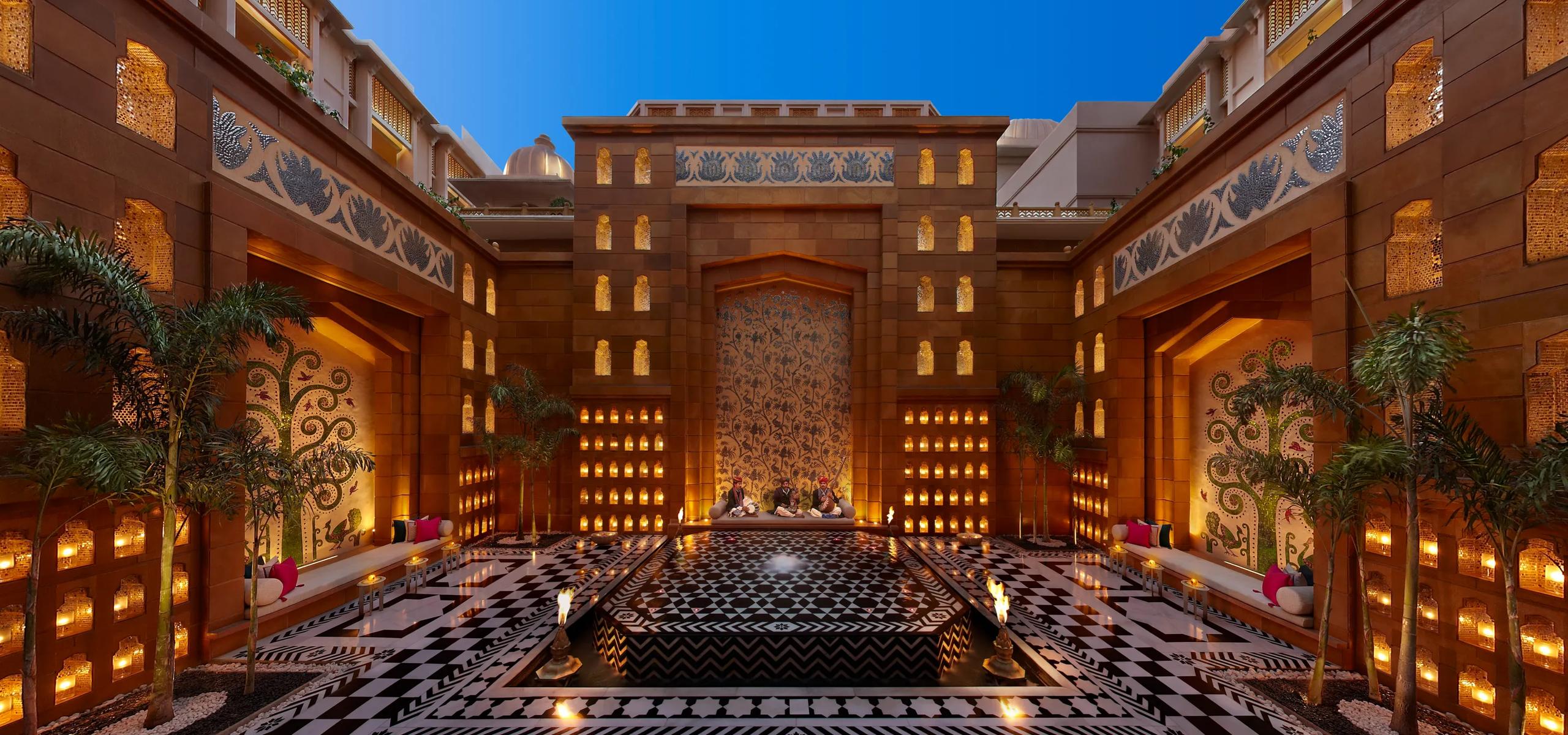 The Leela Palace Udaipur inner courtyard featuring traditional Rajasthani architecture with ornate arches, intricate stone carvings, and a serene reflecting pool